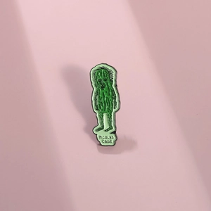 Creative green pickle enamel pin featuring a funny face design on a pink background