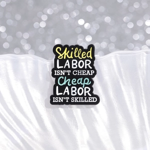 Emaille-Anstecknadel mit Spruch 'Skilled Labor Isn't Cheap' auf Muschelsockel