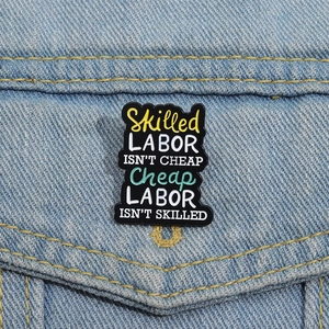 Emaille-Brosche mit Spruch Skilled Labor Isn't Cheap an einer blauen Jeansjacke