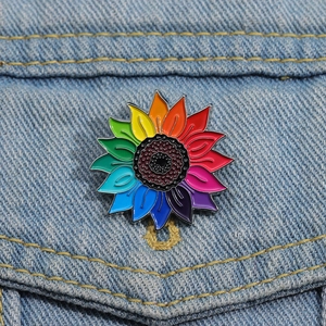 Gros plan d'un pin's émaillé tournesol arc-en-ciel épinglé sur une veste en jean bleu