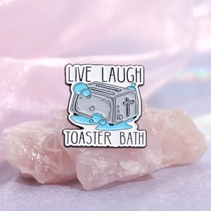 Whimsical enamel toaster bath pin with Live Laugh Toaster Bath text on pink crystal