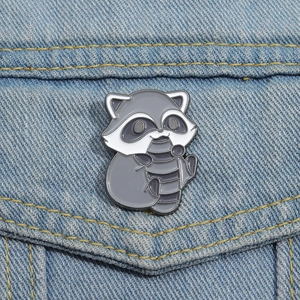 Cute cartoon raccoon enamel pin badge on blue denim jacket pocket accessory