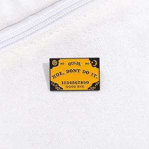 Gros plan du pin's émaillé Ouija jaune avec lettrage gothique sur fond de toile