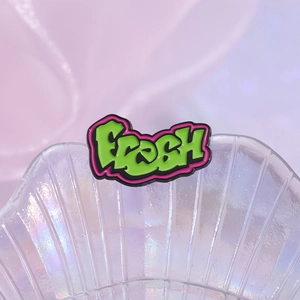 Graffiti style Fresh enamel pin with neon green and pink colors in a shell dish