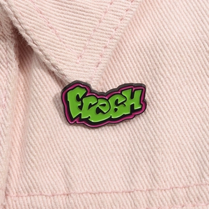 Emaille-Anstecknadel im Graffiti-Stil FRESH in Grün und Rosa auf einer Jeansjacke