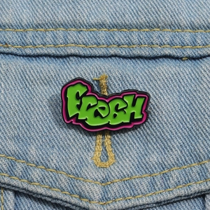Detail der grünen Fresh Graffiti Emaille-Anstecknadel an einer blauen Denim-Jacke
