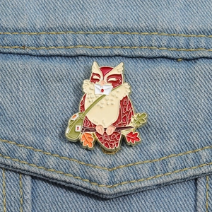 Détail de la broche hibou en émail avec lettre et sac vert sur tissu en denim bleu