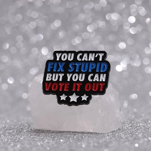 Black enamel pin featuring You Can't Fix Stupid political quote on white crystal