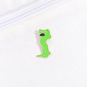 Detailed close-up of funny green enamel long-legged frog pin on white canvas texture