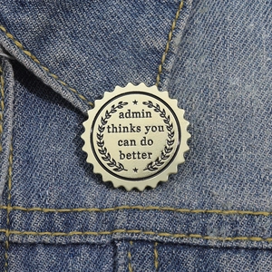 Round serrated enamel brooch with 'admin thinks you can do better' text on blue denim