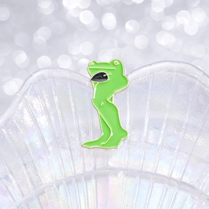 Funny green muscle frog enamel pin with long legs on a white decorative shell tray