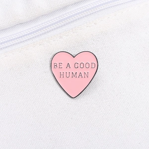 Close-up of pink heart enamel pin with Be A Good Human quote on white canvas bag
