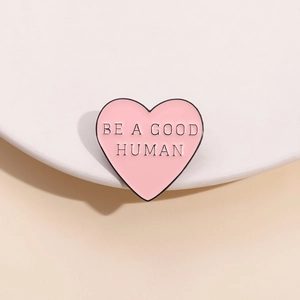 Pink heart enamel brooch with BE A GOOD HUMAN slogan on a minimalist white plate