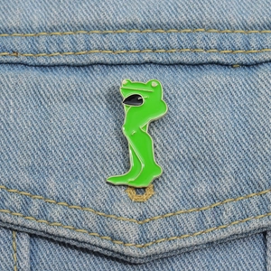 Detailed view of creative long-legged frog enamel pin on a denim jacket background
