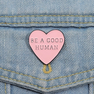 Pink heart enamel pin with 'BE A GOOD HUMAN' quote on a light blue denim jacket