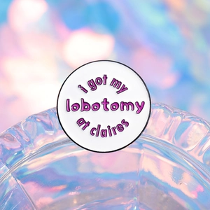 Round white enamel brooch featuring purple 'i got my lobotomy at claires' text design