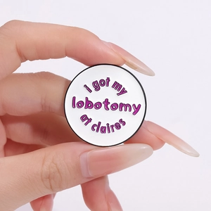 Round enamel pin with Claire's lobotomy text on a white background and purple font