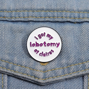 Round white enamel pin with I Got My Lobotomy At Claire's text on denim jacket