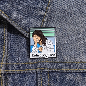 Macro shot of Jesus facepalm enamel pin with I Didn't Say That text on denim