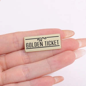 Détail macro d'une broche ticket en métal doré avec lettrage noir et logo gravé