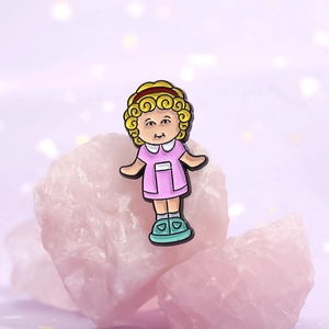 Cartoon enamel pin of a curly-haired girl in a pink dress on a pink mineral background
