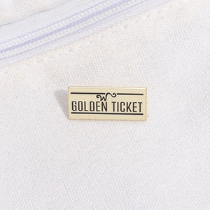 Détail d'une broche en métal Golden Ticket rectangulaire sur une texture de toile