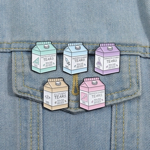 Cute milk carton enamel badges in colorful designs pinned on a blue denim jacket pocket
