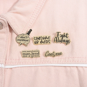 Detail of five vintage metal enamel pins with dark aesthetic slogans on pink denim fabric