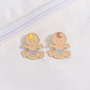 Detailed close-up of cute twin baby enamel pins with purple and blue glitter diapers on canvas
