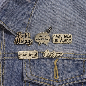 Set of five black and gold enamel mental health quote pins on a denim jacket pocket