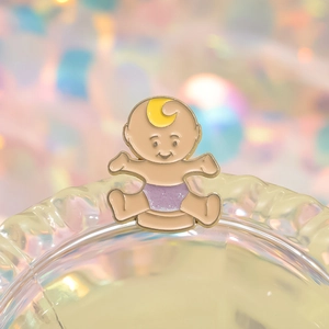 Cute cartoon baby enamel pin with purple glitter diaper on textured glass surface
