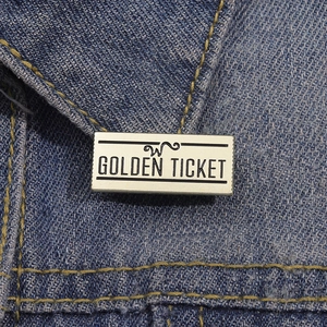 Détail d'un pin's en émail doré en forme de ticket sur une veste en jean bleue