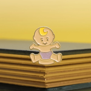 Cute cartoon baby enamel pin with yellow moon and glitter purple diaper on gold-edged book