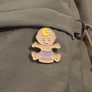 Detail of a cartoon baby enamel pin with purple glitter diaper on olive canvas