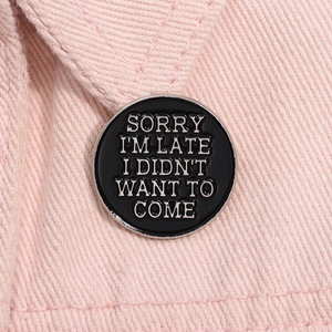 Gros plan du pin's en émail noir avec slogan humoristique sur veste rose