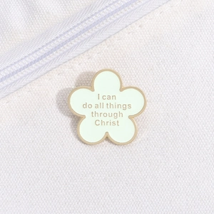 Macro detail of a green flower enamel pin with religious quote on white canvas