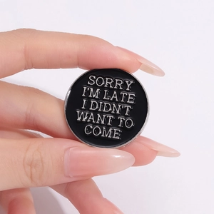 Macro d'un pin's en émail noir avec texte argenté SORRY I'M LATE pour vêtements et sacs