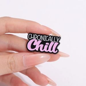 Broche en émail avec base noire et texte 'CHRONICALLY Chill' rose et blanc sur la main