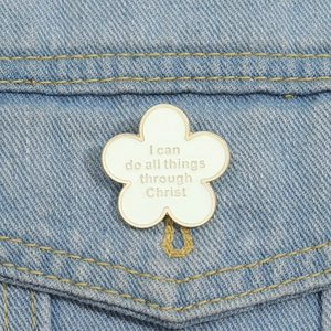 Détail d'un pin's fleur en émail blanc avec texte doré sur une veste en jean