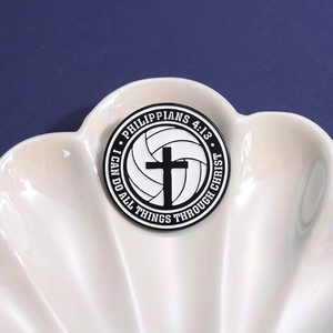 Minimalistischer runder Emaille-Pin mit Kreuz und Volleyball auf weißem Muscheltablett