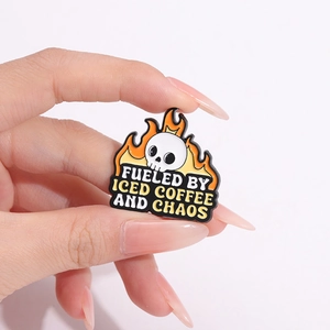 Skull enamel pin featuring Iced Coffee and Chaos slogan held by hand for scale