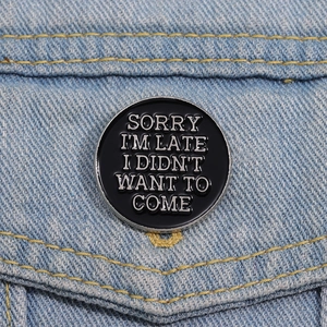 Détail d'une broche ronde en émail noir avec slogan sur une veste en jean bleue