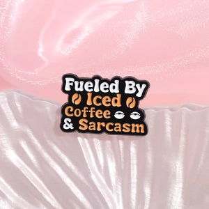Fueled By Iced Coffee & Sarcasm enamel pin badge with skull design on pink background