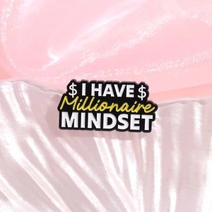 Spilla smaltata Millionaire Mindset su sfondo elegante in seta rosa e conchiglia