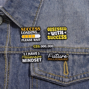 Dettaglio di spille in smalto con citazioni motivazionali sul colletto in denim