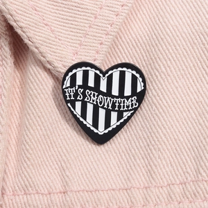 Macro detail of heart-shaped It's Showtime enamel pin on pink denim fabric surface