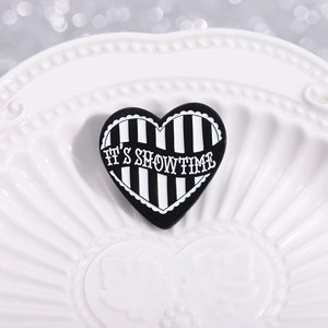 Heart-shaped enamel pin with black and white stripes and It's Showtime lettering