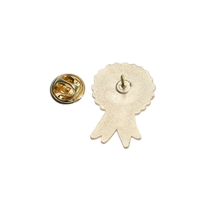 Detail view of the metal badge back featuring a gold-tone butterfly clutch and ribbon pin