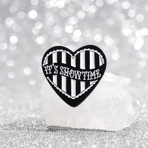 Cartoon black and white striped heart enamel pin with IT'S SHOWTIME slogan