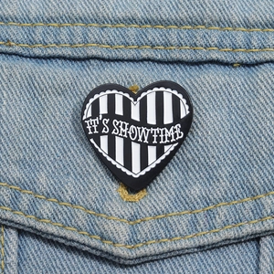 Macro shot of striped heart enamel pin with IT'S SHOWTIME text on denim jacket pocket